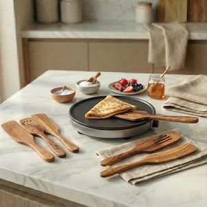 Può includere: Una crepiera con una crepe piegata, spatole di legno e ciotole con ingredienti. Sono presenti anche frutti di bosco freschi e miele, che suggeriscono un tema di colazione o dessert. La scena è ambientata su un piano di lavoro in marmo.