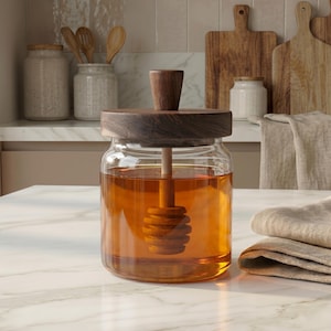May include: A glass honey jar with a wooden lid and dipper. The jar is filled with golden honey. The wooden lid and dipper have a dark brown finish. Kitchen storage and food preparation.
