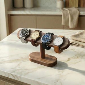 Puede incluir: Un expositor de relojes de madera con cuatro relojes de pulsera. Los relojes tienen correas y esferas de diferentes colores. El expositor es de madera oscura y tiene una base y una parte superior curvada para sujetar los relojes.