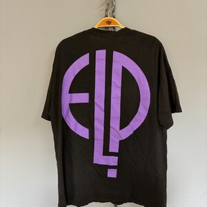 May include: Black t-shirt with a large purple graphic on the back. The graphic is a stylized design of the letters "E", "L", and "P". The shirt is hanging on a wooden hanger.