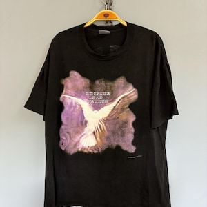 May include: Black t-shirt with a white bird graphic and the text "Jefferson Airplane". The bird has outstretched wings against a purple and brown background. The t-shirt is hanging on a gold hanger.