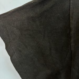 May include: Close-up of a black t-shirt sleeve. The fabric appears to be a soft cotton blend, with visible texture and subtle variations in the dark colour. The sleeve's edge is neatly hemmed with a visible seam.