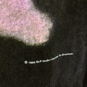 May include: Close-up of a black t-shirt with a faded purple design. The text "&copy; 1992 ELP Under License To Brockum" is printed in white along the bottom edge of the shirt.