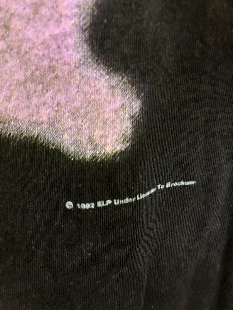 May include: Close-up of a black t-shirt with a faded purple design. The text "&copy; 1992 ELP Under License To Brockum" is printed in white along the bottom edge of the shirt.