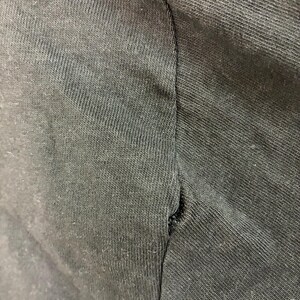 May include: Close-up of a dark grey t-shirt sleeve, showing the seam and fabric texture. The fabric has a ribbed texture, and the seam is slightly frayed.