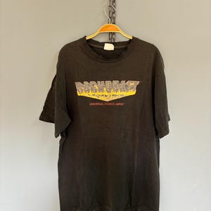 May include: Dark grey t-shirt featuring the yellow and orange graphic "DARKDRAG" with the text "UNIVERSAL STUDIOS JAPAN" underneath. The shirt is suspended on a gold hanger.