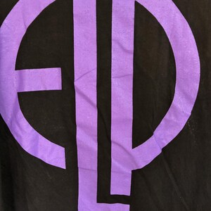 May include: Black t-shirt with a large, purple graphic design. The graphic is a monogram or logo, with the letters "E", "L", and "P" in a bold, sans-serif font. The design is centrally placed on the shirt.
