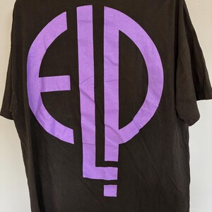 May include: Black t-shirt featuring a large purple graphic on the back. The graphic is a stylized design with the letters "E", "L", and "P" in a circular and vertical arrangement. The shirt has short sleeves and a crew neck.