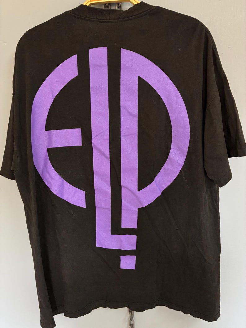 May include: Black t-shirt featuring a large purple graphic on the back. The graphic is a stylized design with the letters "E", "L", and "P" in a circular and vertical arrangement. The shirt has short sleeves and a crew neck.