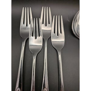 Op de afbeelding: Een verzameling roestvrijstalen vorken met een decoratief ontwerp op het handvat. De vorken zijn gerangschikt op een donkere ondergrond, waarbij hun gepolijste afwerking en tanden worden benadrukt. Het bestek maakt waarschijnlijk deel uit van een eetservies.