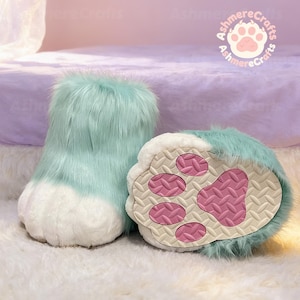 May include: A pair of furry, light blue and white paw-shaped slippers. The slippers have a plush, textured appearance with a pink paw pad design on the soles. The slippers are designed to resemble animal paws.