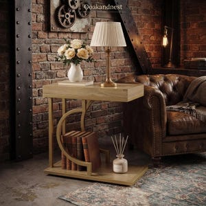May include: A rectangular side table with a light wood finish and a gold metal frame featuring a curved support. The table holds a white vase with cream flowers, a pleated lampshade on a gold base, a stack of books, and a small reed diffuser.