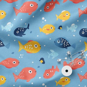 Puede incluir: Tela azul claro con un estampado repetido de peces de dibujos animados coloridos. Los peces son rojos, amarillos y azules, con detalles blancos. El diseño incluye pequeñas burbujas y algunos peces pequeños de color azul oscuro.