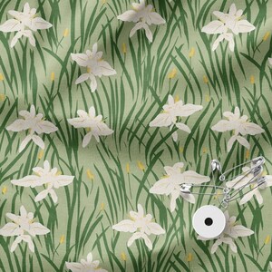 Puede incluir: Una tela verde claro con un patrón repetido de flores blancas y hierba verde. Varios imperdibles plateados y un botón blanco están sobre la tela.