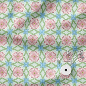 May include: A light blue fabric featuring a repeating pattern of pink lotus-like flowers and small blue four-petaled blossoms connected by green vines. A white circular button and several silver metal safety pins are placed on the fabric.