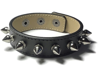 May include: Black leather bracelet with silver metal spikes. The bracelet has a brown leather strap with three silver metal snaps.