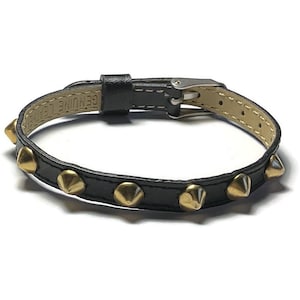May include: Black leather bracelet with gold-colored cone studs. The bracelet has a silver-tone buckle and is labeled "GENUINE LEATHER". A stylish accessory for adding a touch of edge to any outfit.
