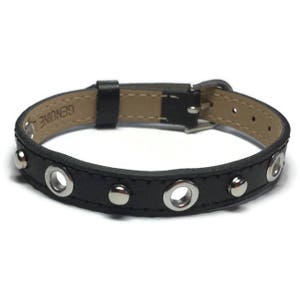 May include: Black leather bracelet with silver grommets and a buckle closure. The bracelet has the word "GENUINE" embossed on the leather.