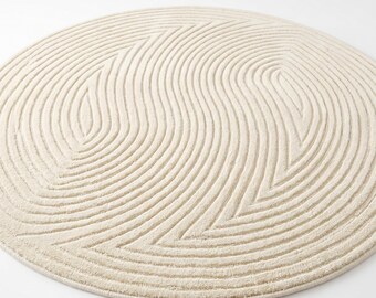 May include: A round, cream-coloured rug featuring a textured, raised pattern of curved, wave-like lines that create a symmetrical design across the surface. The logo for Mirzapur Rug Hub is visible in the bottom right corner of the image.