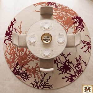 Puede incluir: Una alfombra circular con fondo crema y un patr&oacute;n abstracto similar al coral en tonos naranja y rojo oscuro. Una mesa de comedor redonda con cuatro sillas se sit&uacute;a sobre la alfombra, con platos blancos, cubiertos y un cuenco dorado.
