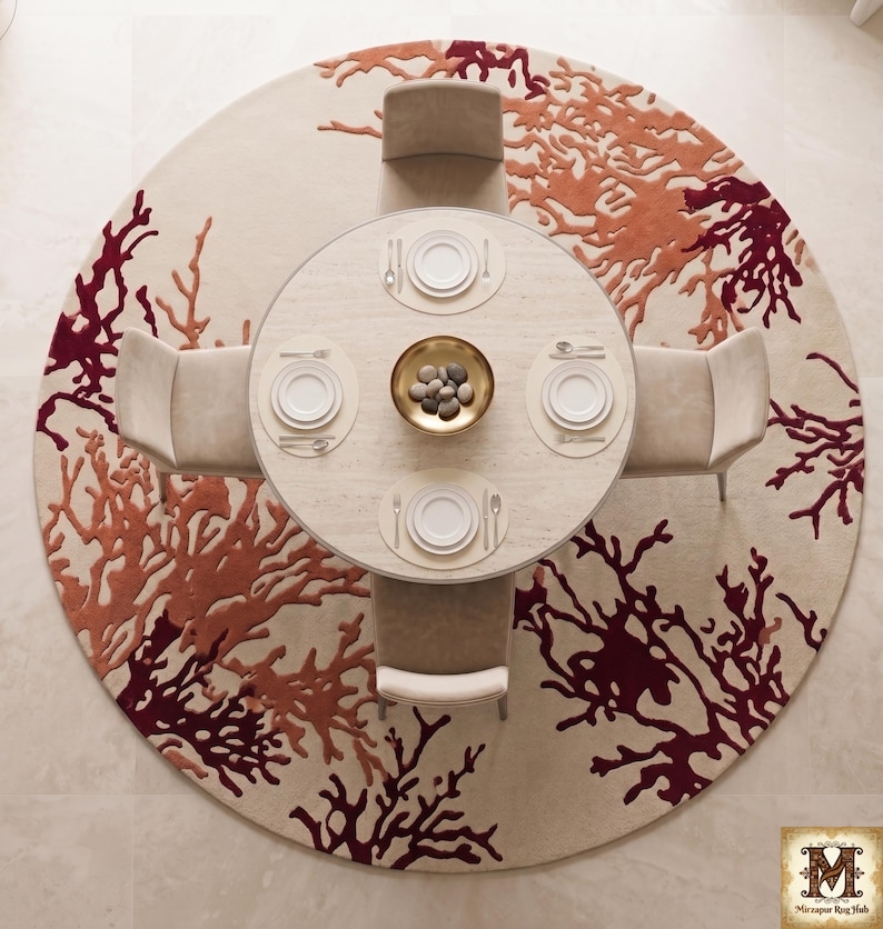 Puede incluir: Una alfombra circular con fondo crema y un patr&oacute;n abstracto similar al coral en tonos naranja y rojo oscuro. Una mesa de comedor redonda con cuatro sillas se sit&uacute;a sobre la alfombra, con platos blancos, cubiertos y un cuenco dorado.