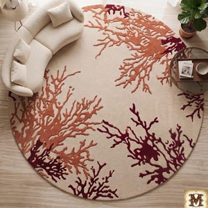 Puede incluir: Una alfombra circular grande con fondo color crema y un patr&oacute;n texturizado en relieve de formas de coral ramificadas en tonos naranja quemado y granate profundo. El dise&ntilde;o se extiende por toda la superficie con un motivo org&aacute;nico.