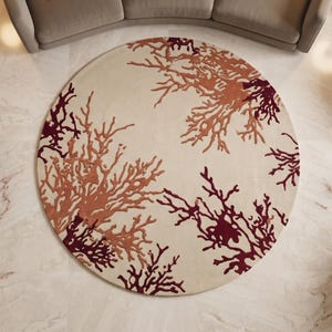 Puede incluir: Una alfombra circular con un fondo de color crema y un patr&oacute;n repetitivo de ramas similares al coral en tonos burdeos intenso, rojo oscuro y naranja apagado. El dise&ntilde;o se extiende por toda la superficie de la alfombra redonda.