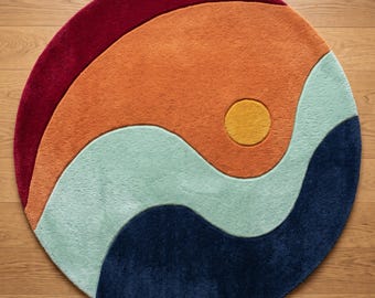 May include: A circular area rug featuring a colour-blocked design with curved, wave-like sections in deep red, burnt orange, light mint green, and navy blue. A small, solid yellow circle is positioned within the orange section. A logo reads Mirzapur Rug Hub.