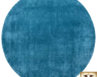 May include: A circular rug in a solid deep teal colour with a plush, shaggy texture. The surface features a dense pile of soft fibres. In the bottom right corner, there is a square logo containing the letter M and the text Mirzapur Rug Hub.