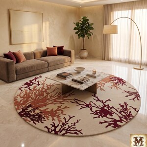 Puede incluir: Una alfombra circular grande con una base de color crema y un intrincado patr&oacute;n de ramas que recuerda al coral en tonos burdeos intenso y naranja quemado. La alfombra est&aacute; colocada sobre un suelo pulido bajo una mesa de centro de m&aacute;rmol.