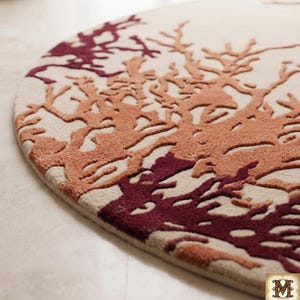 Puede incluir: Una alfombra circular con una base de color crema y un patr&oacute;n texturizado en relieve de ramas similares al coral en tonos burdeos profundo y naranja quemado. El dise&ntilde;o cubre la superficie con formas org&aacute;nicas ramificadas.