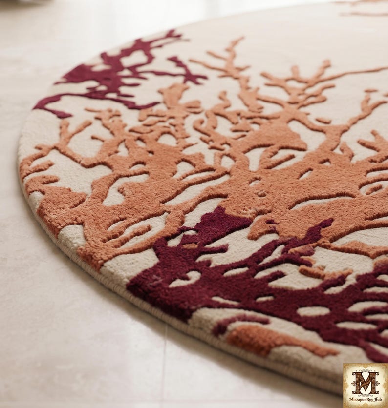 Puede incluir: Una alfombra circular con una base de color crema y un patr&oacute;n texturizado en relieve de ramas similares al coral en tonos burdeos profundo y naranja quemado. El dise&ntilde;o cubre la superficie con formas org&aacute;nicas ramificadas.