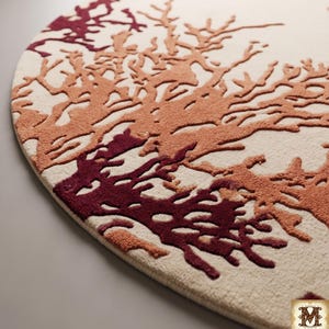 Puede incluir: Una alfombra circular con una base de color crema y un patr&oacute;n texturizado en relieve de ramas similares a corales en tonos burdeos profundo y naranja quemado. El dise&ntilde;o incluye el logotipo de Mirzapur Rug Hub en la esquina inferior derecha.