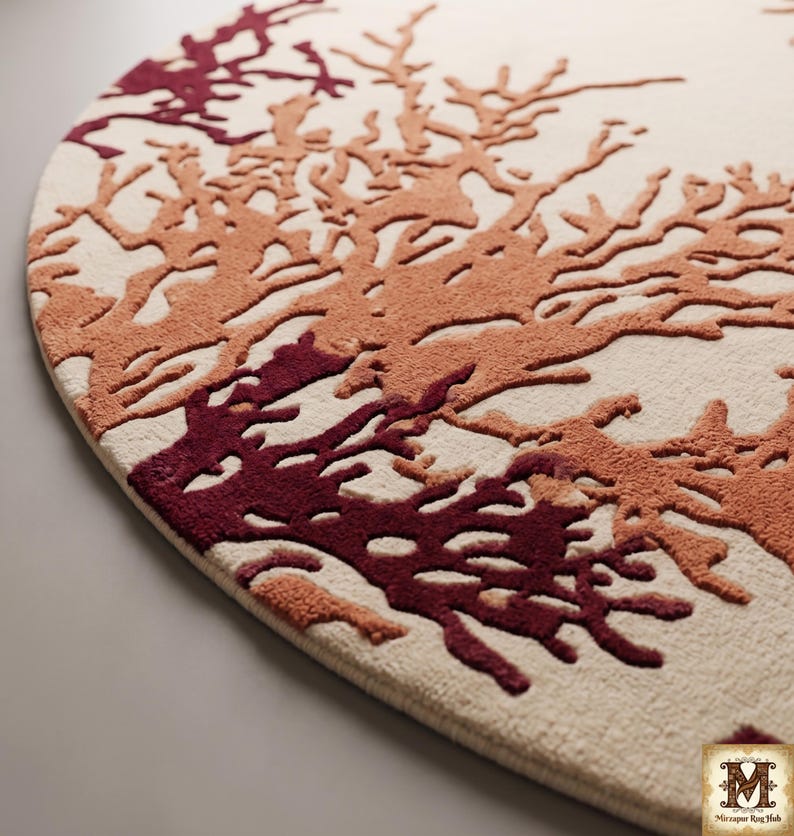 Puede incluir: Una alfombra circular con una base de color crema y un patr&oacute;n texturizado en relieve de ramas similares a corales en tonos burdeos profundo y naranja quemado. El dise&ntilde;o incluye el logotipo de Mirzapur Rug Hub en la esquina inferior derecha.