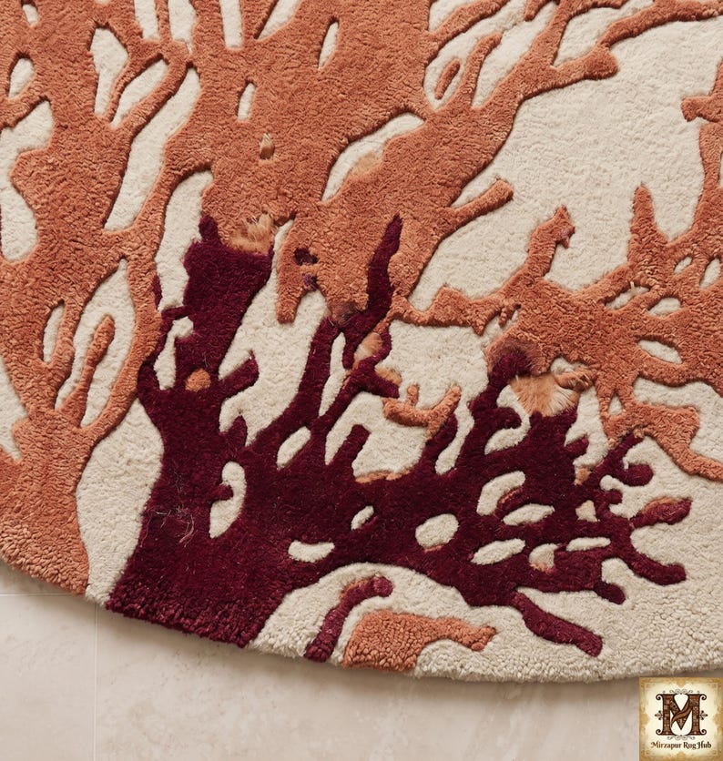 Puede incluir: Una alfombra circular con textura de pelo largo y mechones sobre una base de color crema. El dise&ntilde;o muestra un patr&oacute;n intrincado de ramas que recuerdan al coral en tonos naranja quemado y granate profundo, creando un fuerte contraste visual.