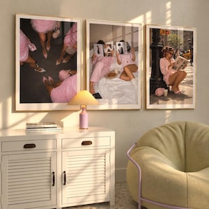 May include: Three framed wall art prints featuring pink-themed photography. The left print shows legs in pink skirts, the center print shows two people reading magazines in bed, and the right print shows a person reading a newspaper on a city street.