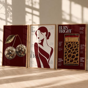 May include: Three framed wall art prints in a deep red colour palette. The left print shows two disco ball cherries with a gold leaf. The centre print features a stylised silhouette of a person with the text "LESS IS MORE" and "IN HER ERA". The right print displays a matchbox with a leopard print pattern and the text "BURN BRIGHT".