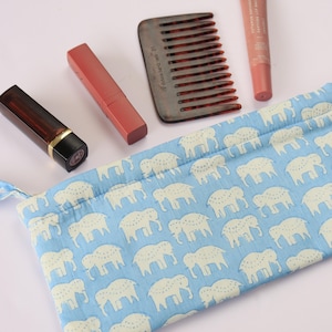 Könnte beinhalten: Ein hellblauer Stoffbeutel mit einem sich wiederholenden weißen Elefantenmuster, begleitet von einem dunkelbraunen Haarkamm, einem matten roten Lippenstift und einer kleinen Tube getönter Lippenpflege mit dem Text Vitamin Infused Peptide Lip Balm.