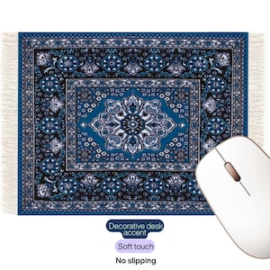 Puede incluir: Alfombrilla de escritorio con estampado azul y blanco con borde con flecos, que se asemeja a una alfombra en miniatura. La alfombrilla tiene texto que dice "Decorative desk accent", "Soft touch" y "No slipping". Un ratón de ordenador blanco está en primer plano.