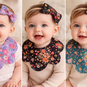 May include: Three babies wearing floral bibs and matching headbands. The bibs are in purple, black, and teal, each with a different floral pattern. The babies are smiling and wearing white onesies.