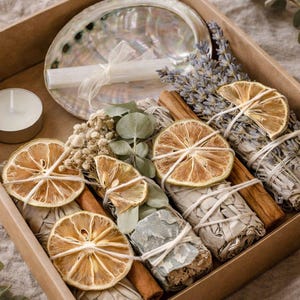May include: A brown cardboard box filled with a variety of items for spiritual practices. Includes a polished abalone shell, dried sage bundles, dried orange slices, cinnamon sticks, a small candle, and sprigs of lavender and eucalyptus.