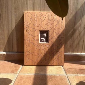 May include: A wooden art piece, rectangular in shape, featuring a central framed image. The wood displays a natural grain and is etched with a branching design. The inner image shows a star and bird silhouette on a dark backdrop.