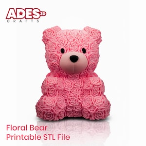 以下が含まれることがあります： バラ模様のピンク色の花のクマの彫刻。クマは黒い目と薄いピンク色の鼻をしています。「Floral Bear Printable STL File」というテキストが下にあります。「ADES Crafts」のロゴが左上にあります。