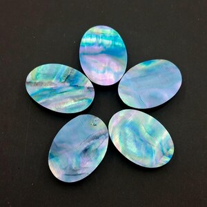 Puede incluir: Cinco cabujones ovalados iridiscentes en tonos azules, verdes y morados, dispuestos en forma de estrella. Las superficies pulidas reflejan la luz, mostrando patrones naturales. Estas gemas son probablemente para joyería o artesanía.