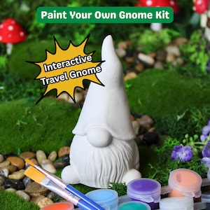 May include: A white ceramic gnome figure with a long beard and pointed hat, part of a paint-your-own kit. The kit includes paint pots, brushes, and the text "Paint Your Own Gnome Kit" and "Interactive Travel Gnome".