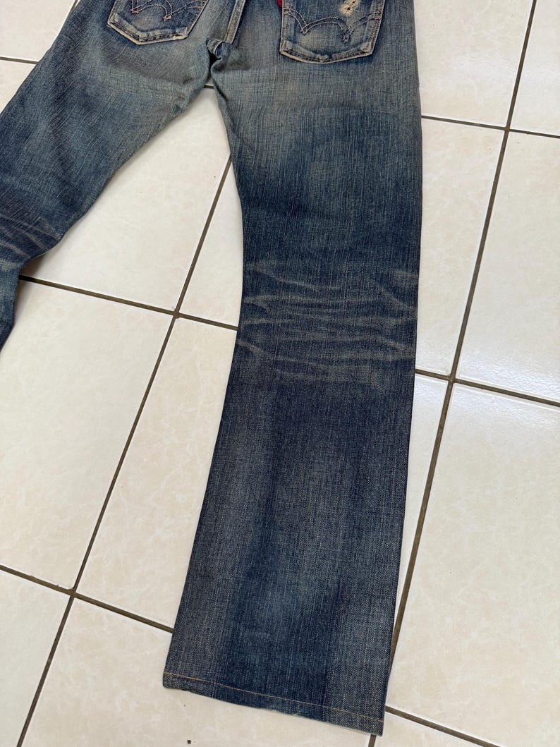 May include: Faded blue denim jeans with a worn appearance. The jeans have a classic five-pocket design, with visible wear and tear, including distressed areas and fading. The denim has a medium wash with darker shading on the legs.