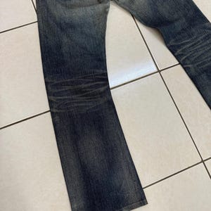 May include: Faded blue denim jeans with a classic five-pocket design. The jeans show signs of wear and fading, with a slightly flared leg. The back pockets feature a distinctive stitch pattern. The jeans are made of durable denim.