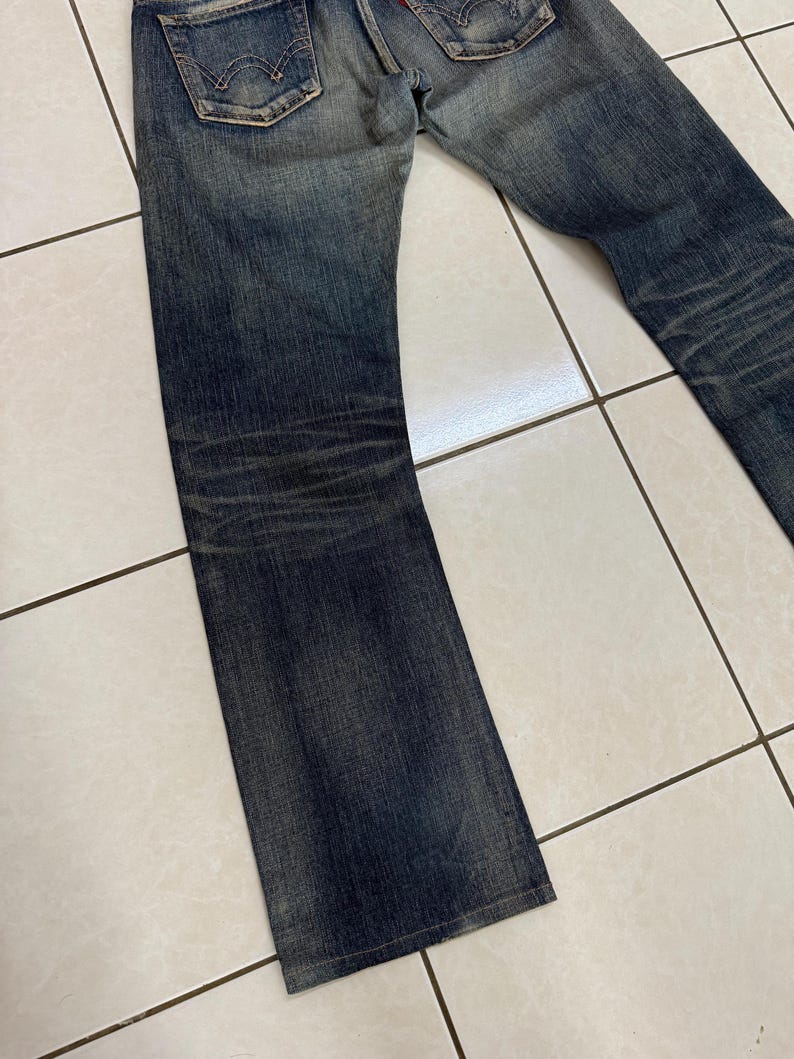 May include: Faded blue denim jeans with a classic five-pocket design. The jeans show signs of wear and fading, with a slightly flared leg. The back pockets feature a distinctive stitch pattern. The jeans are made of durable denim.