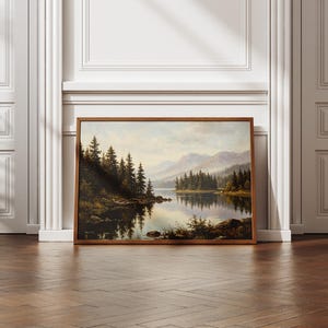May include: A rectangular landscape painting in a wooden frame depicting a serene lake surrounded by dense evergreen forests and distant mountains under a soft, overcast sky, with the reflection of the trees visible on the calm water surface.
