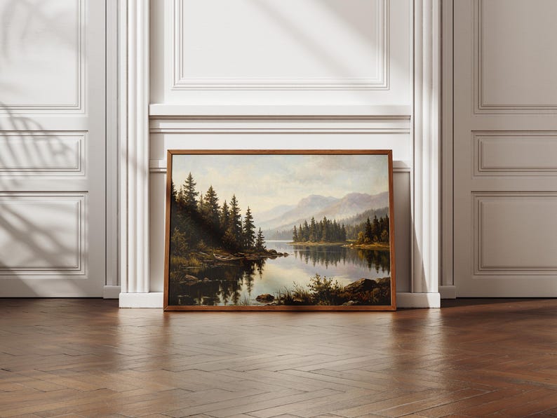 May include: A rectangular landscape painting in a wooden frame depicting a serene lake surrounded by dense evergreen forests and distant mountains under a soft, overcast sky, with the reflection of the trees visible on the calm water surface.